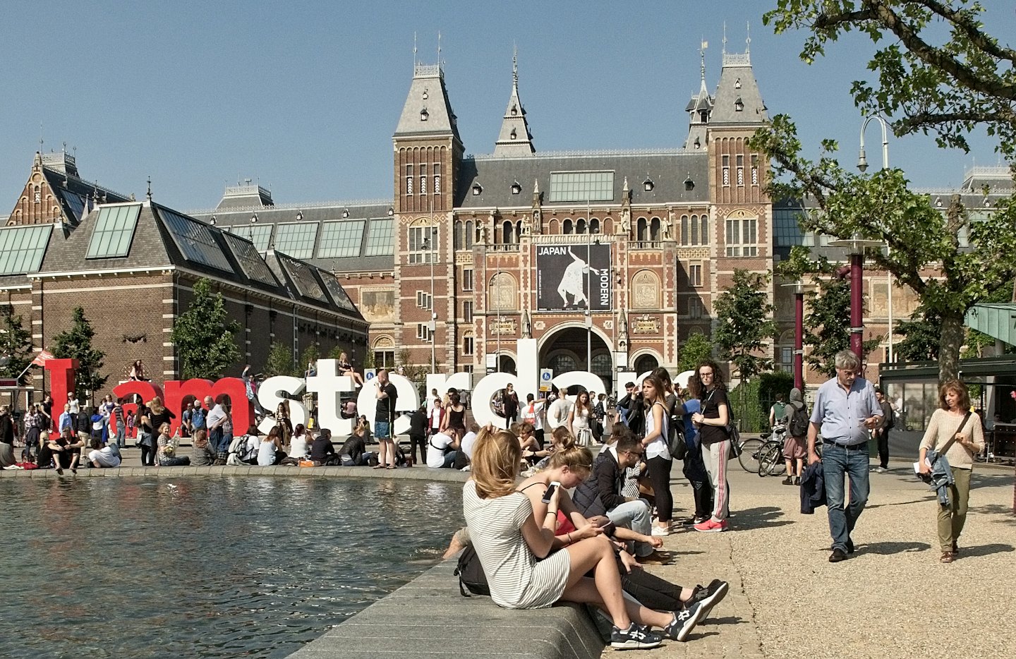 Mensen verzamelen zich bij het Amsterdamse bord bij een historisch gebouw.