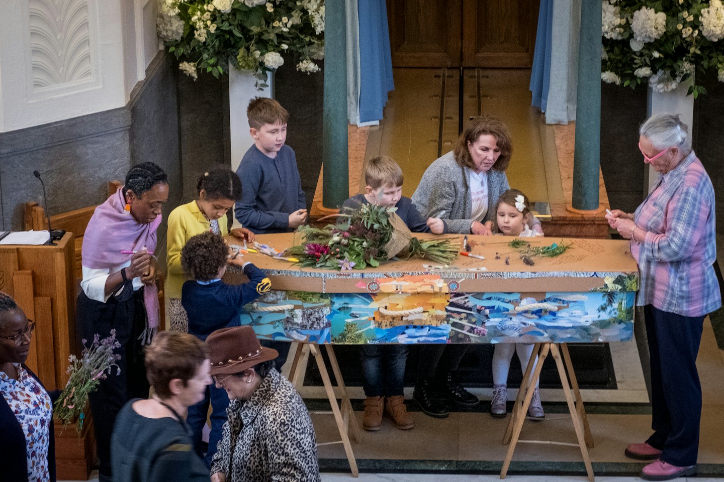 Diverse groep mensen die kunst maken aan een grote tafel.
